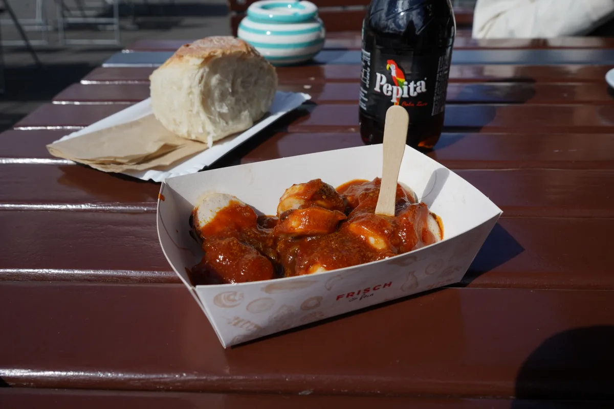 Currywurst, die auf dem Tisch steht, mit viel Sauce darüber.